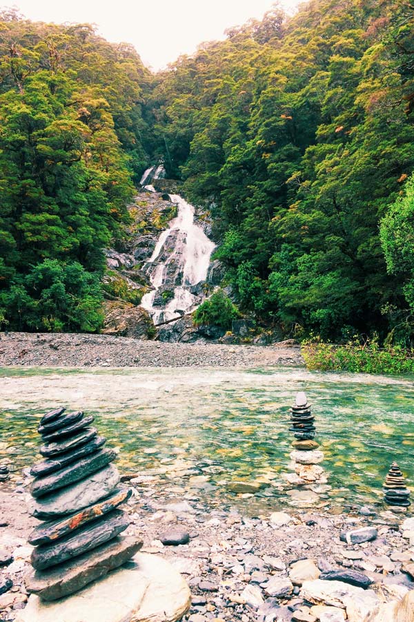 Fantails Falls in New Zealand in the background with rock stacks by humans in the foreground